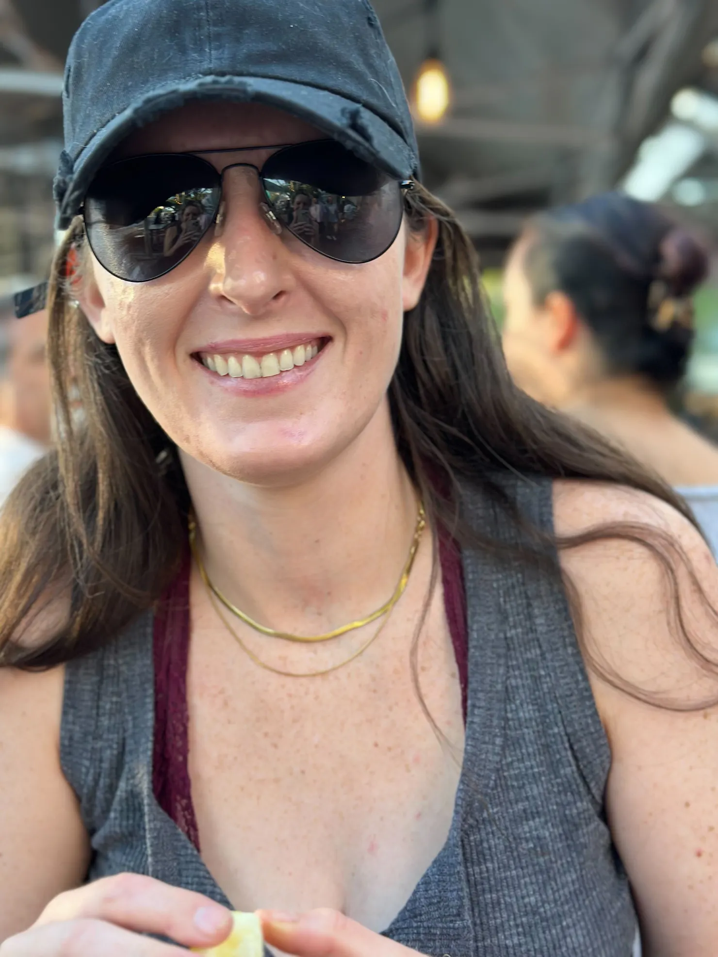 Portrait of Claire Sylvester smiling in a baseball cap and aviator sunglasses