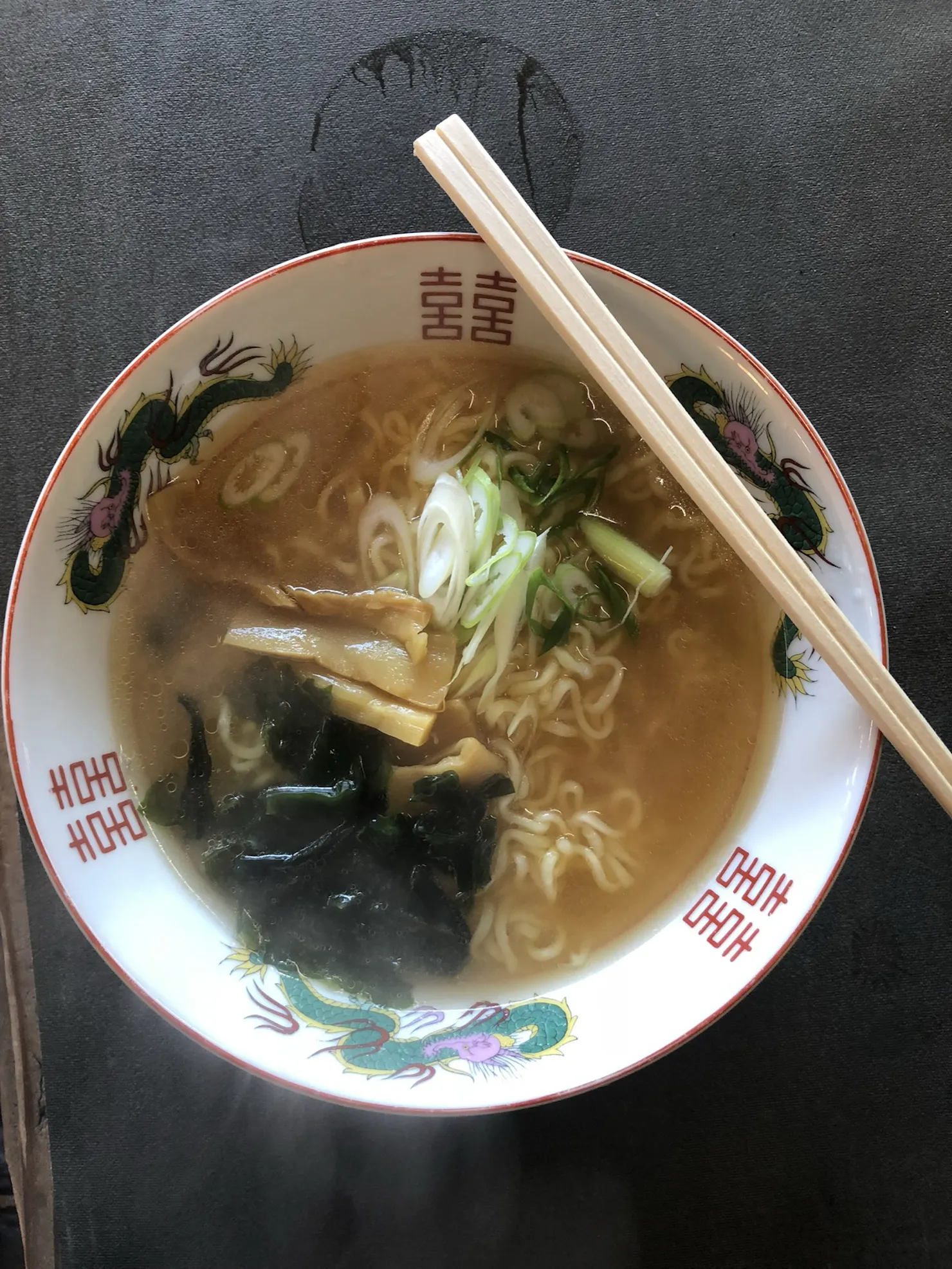 Bowl of ramen topped with seaweed, bamboo shoots and green onions, with chopsticks resting on the rim