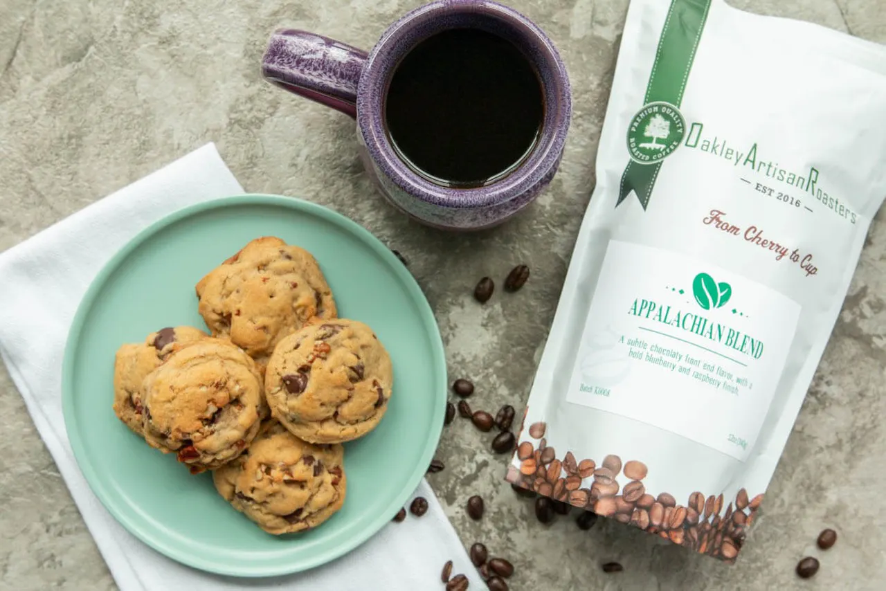 Overhead shot of chocolate chip cookies on a green plate, a mug of black coffee and a bag of Oakley Artisan Roasters Appalachian Blend
