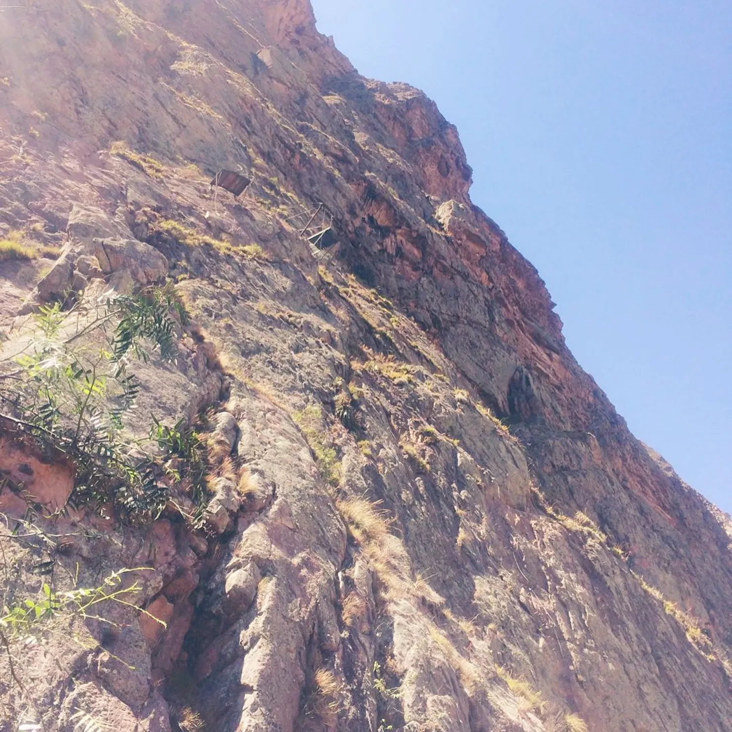 Looking up a sheer rock face in the Sacred Valley with small climbing pods anchored high on the cliff