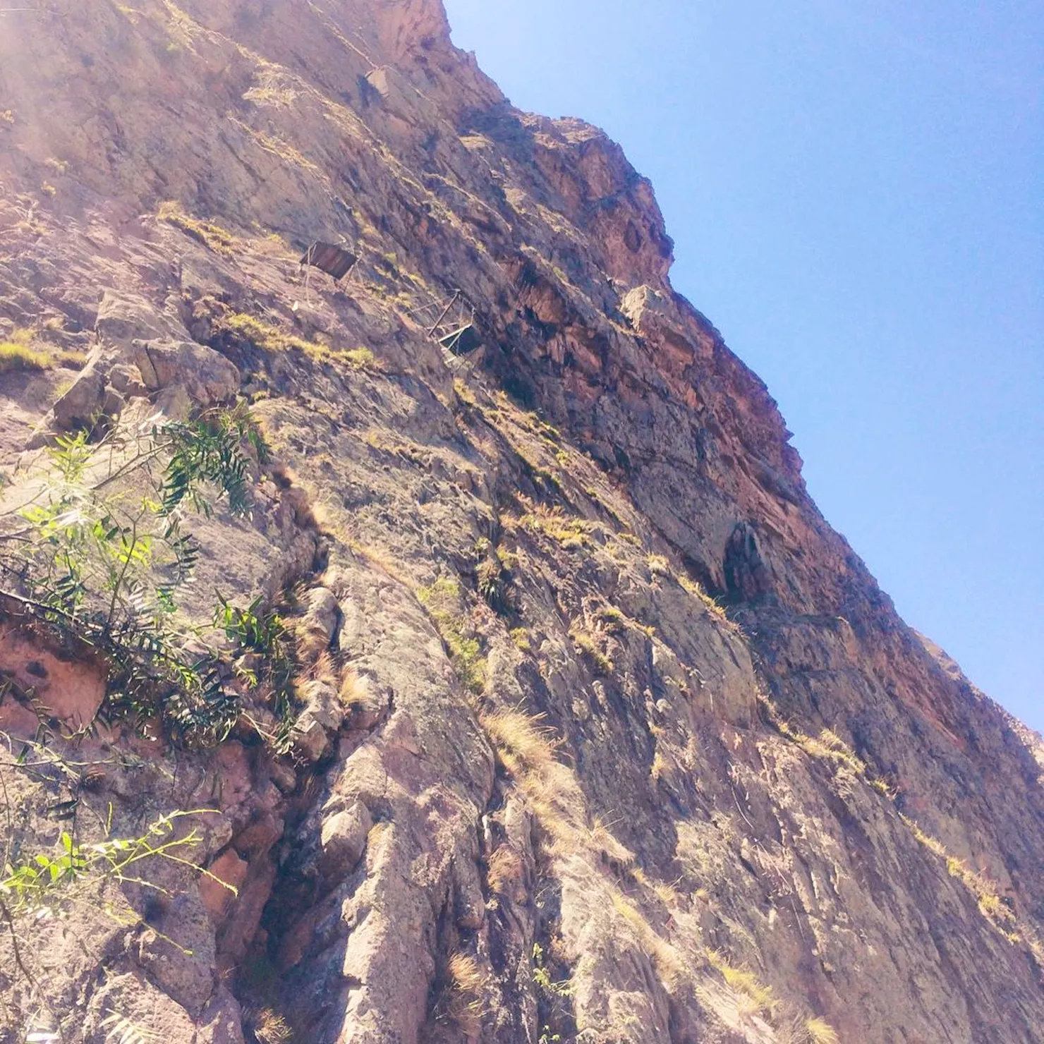 Looking up a sheer rock face in the Sacred Valley with small climbing pods anchored high on the cliff