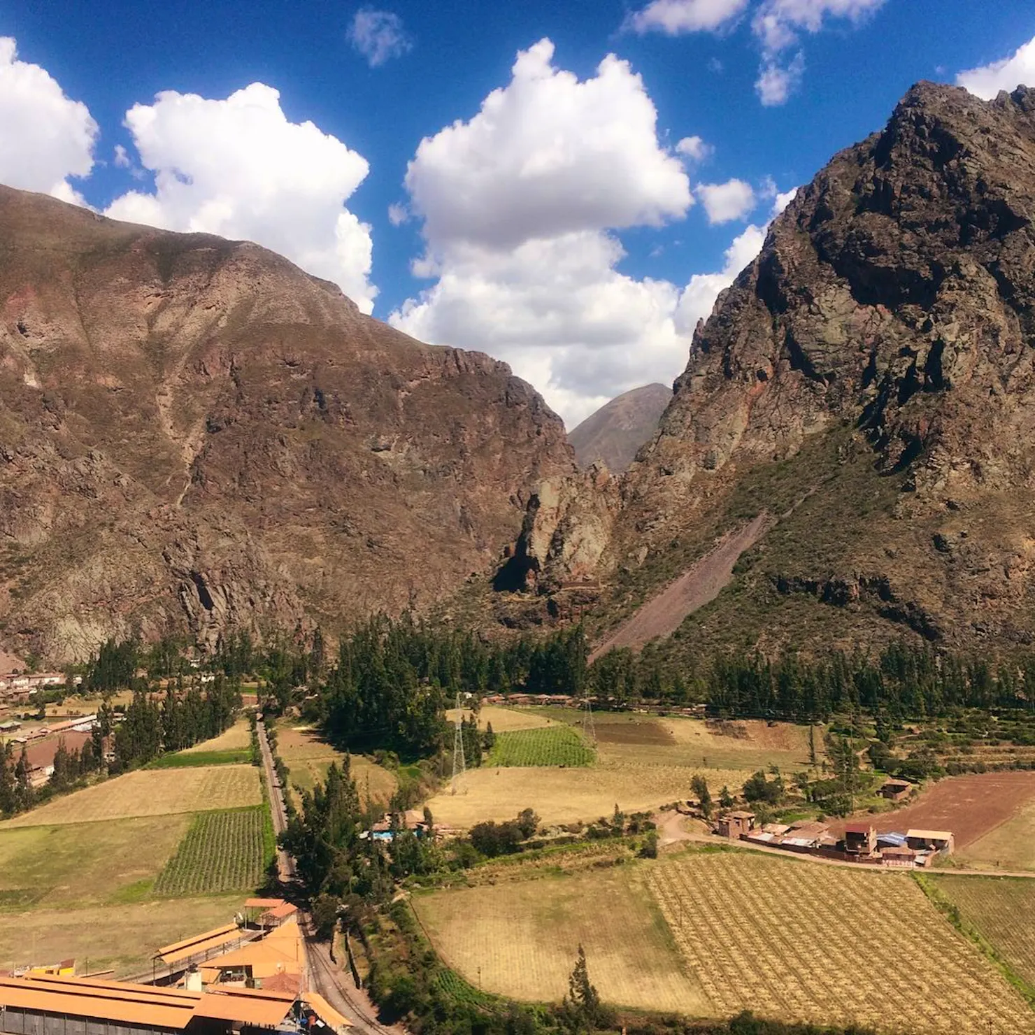 Andean peaks rising over farmland and a small village in the Sacred Valley under a blue sky