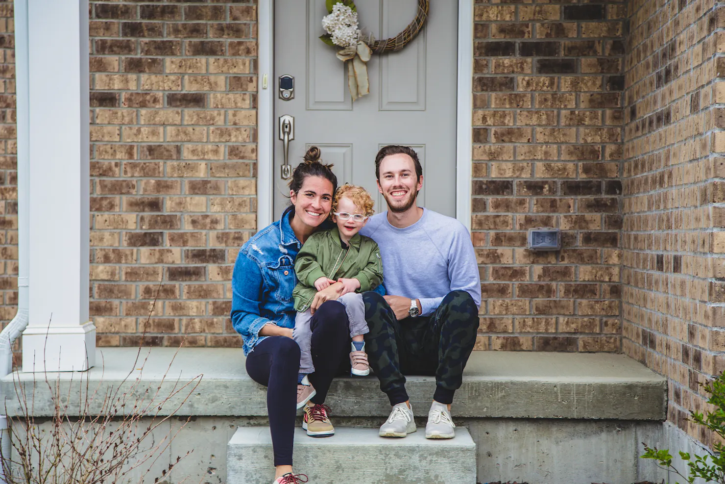 Sarah Shiffman, her husband and their son Emerson sitting together on the front steps of a brick house