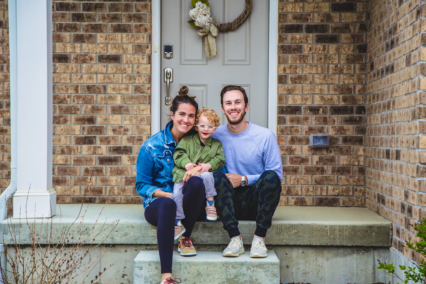 Sarah Shiffman, her husband and their son Emerson sitting together on the front steps of a brick house