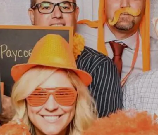 Paycor employees in orange props and novelty glasses posing in a photo booth