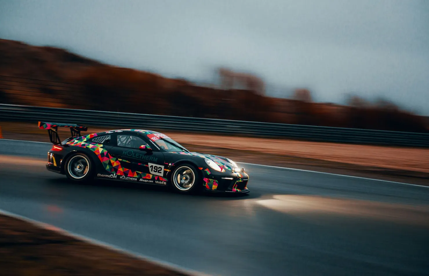 Colorfully wrapped race car speeding along a wet track, a nod to Rudo's favorite game, iRacing