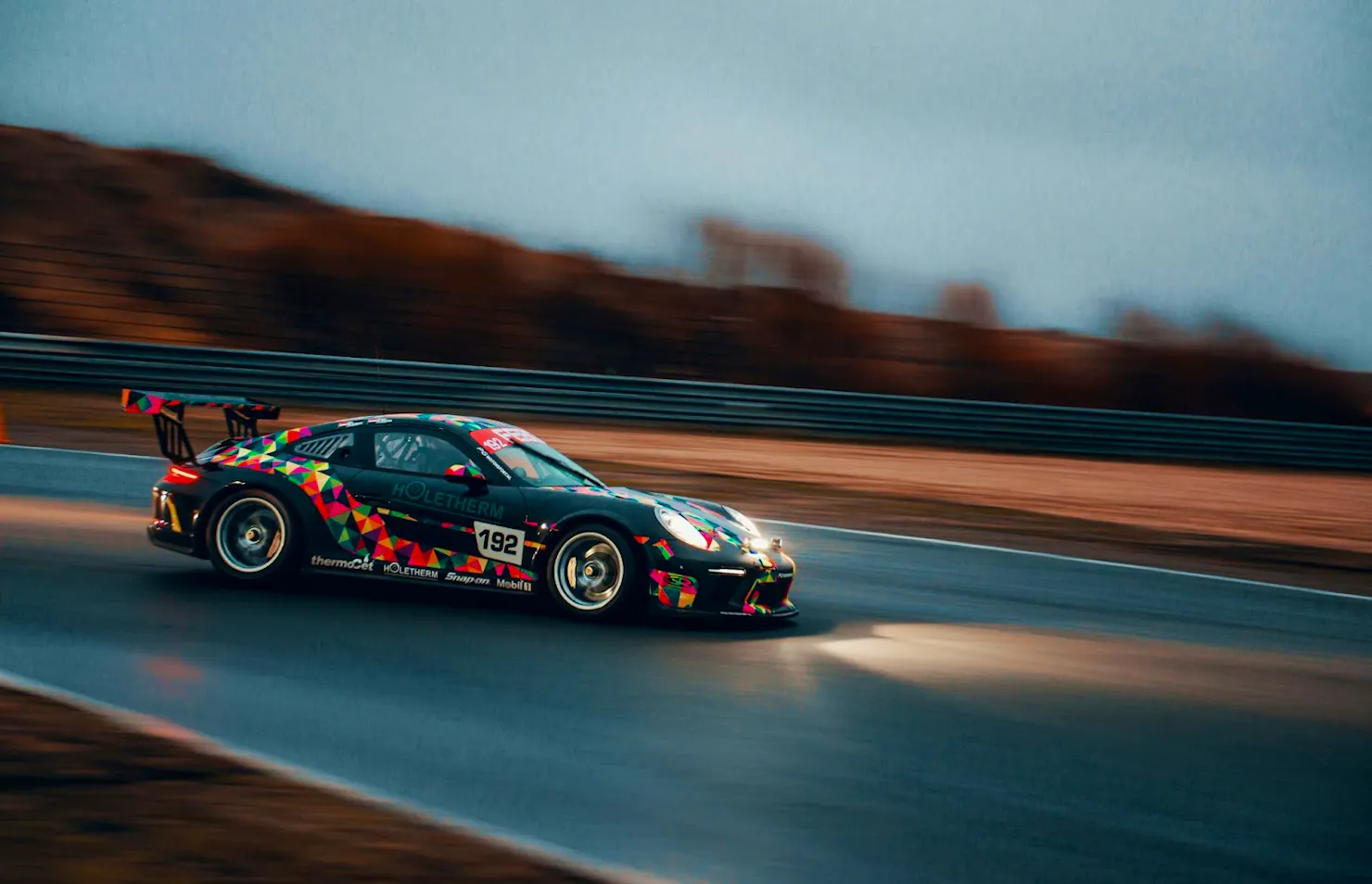 Colorfully wrapped race car speeding along a wet track, a nod to Rudo's favorite game, iRacing