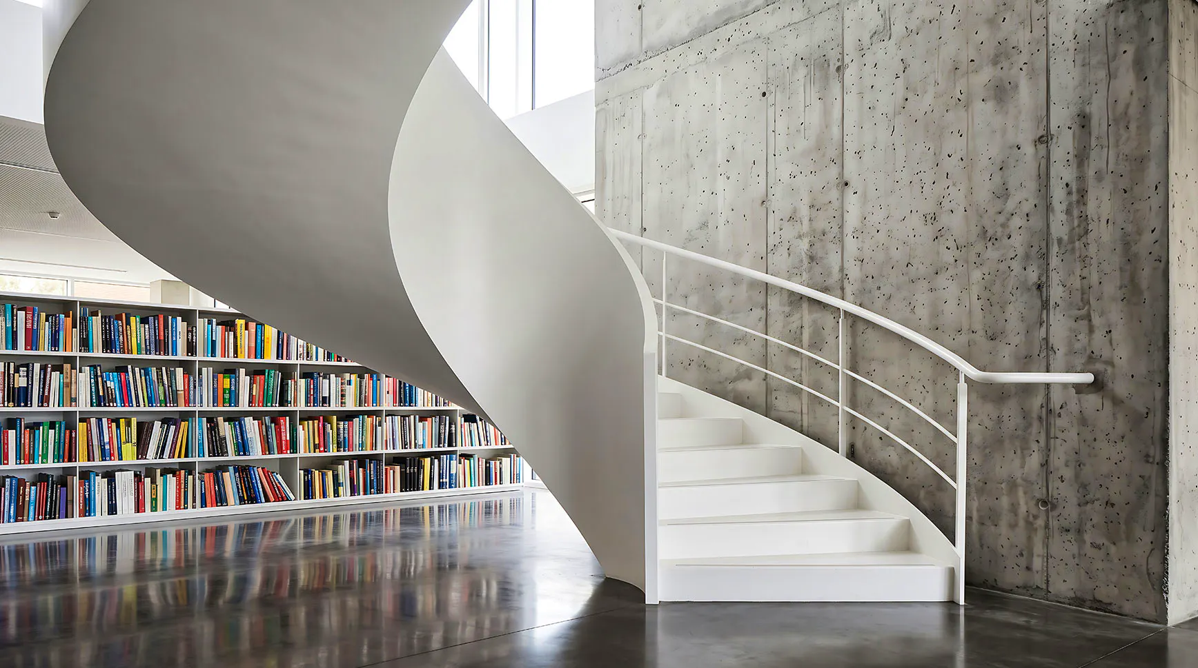 White spiral staircase in a modern library beside a wall of colorful bookshelves