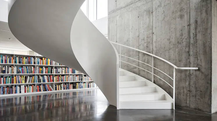 White spiral staircase in a modern library beside a wall of colorful bookshelves