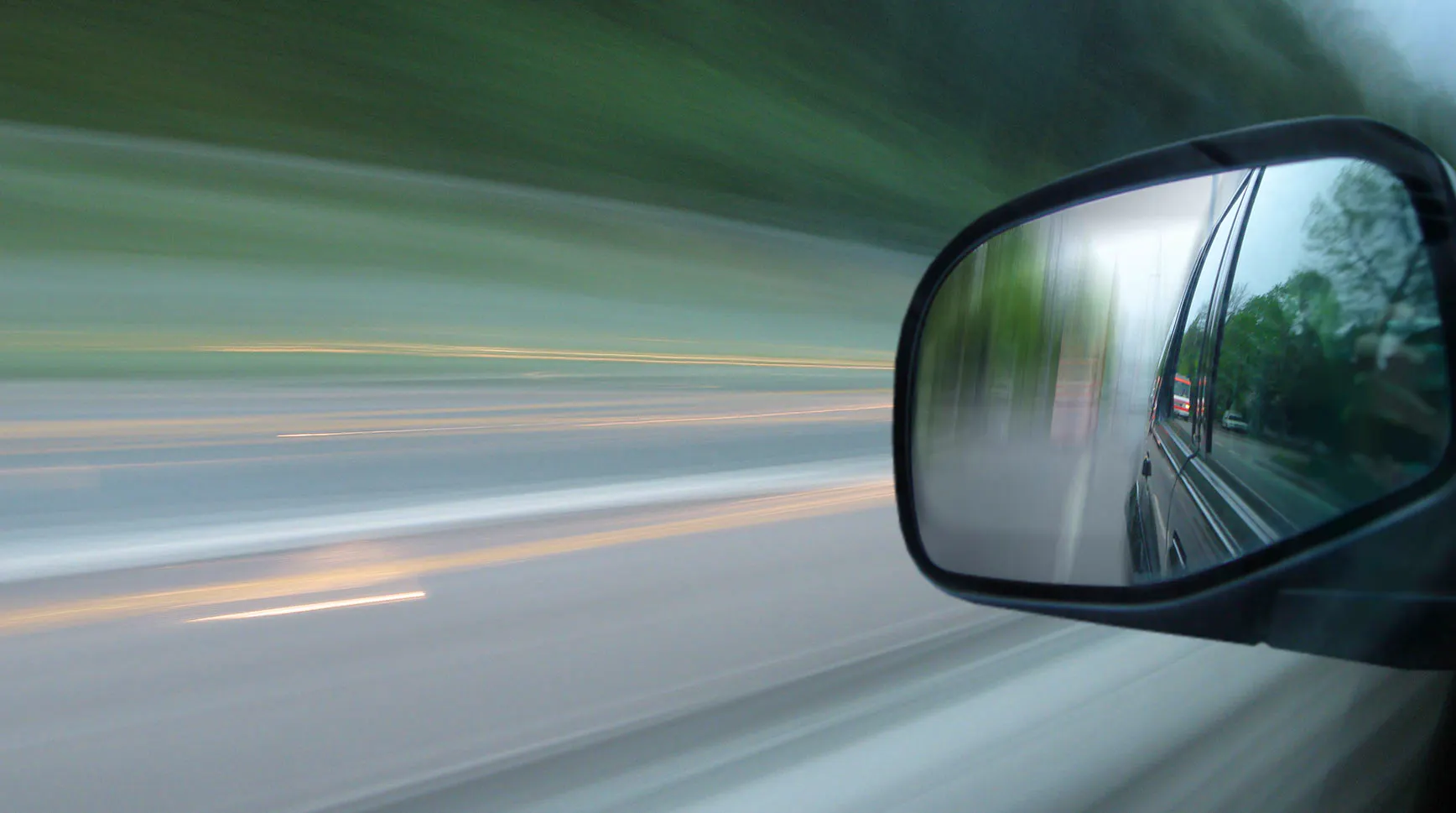 Motion-blurred view from a moving car with the road behind reflected in the side mirror