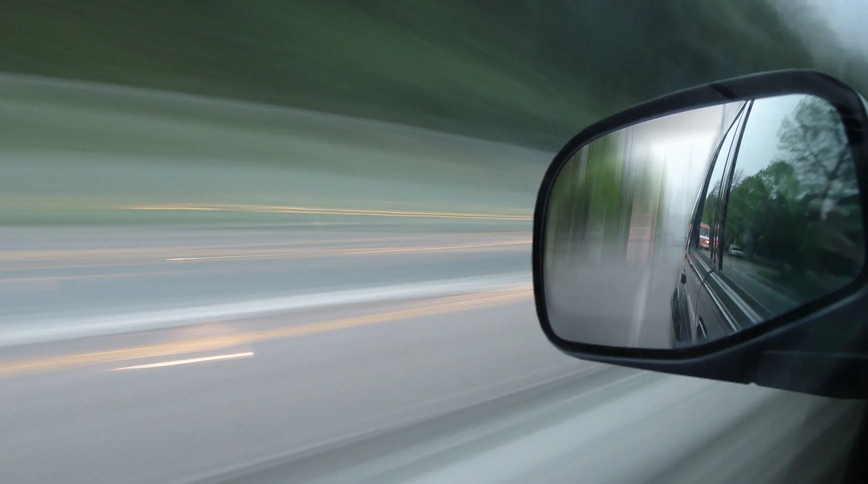 Motion-blurred view from a moving car with the road behind reflected in the side mirror