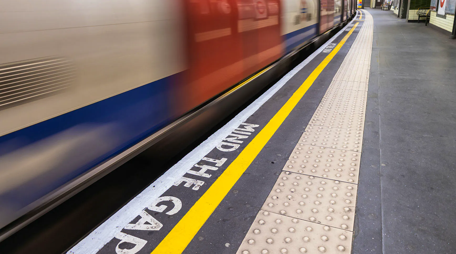 Blurred London Underground train passing a platform edge painted with the words Mind the Gap